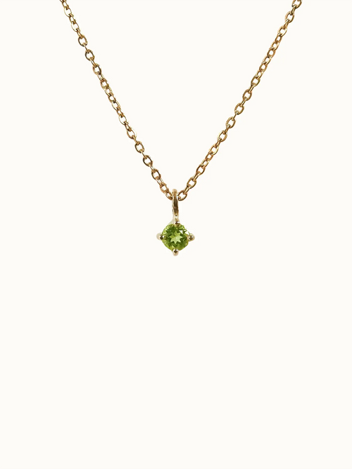 Gold necklace with a green gemstone pendant on a white background