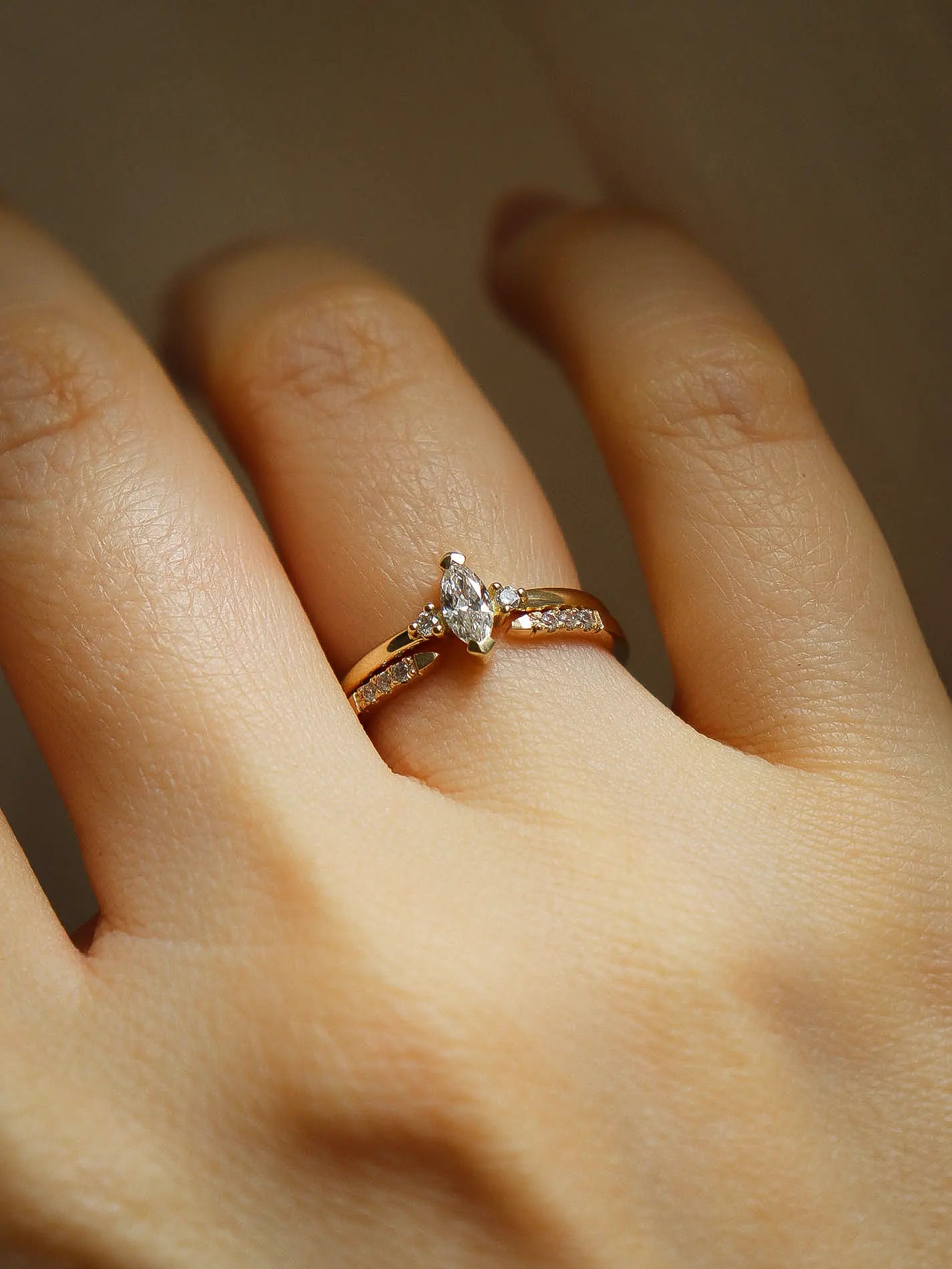 Gold ring with a diamond on a person's finger against a neutral background