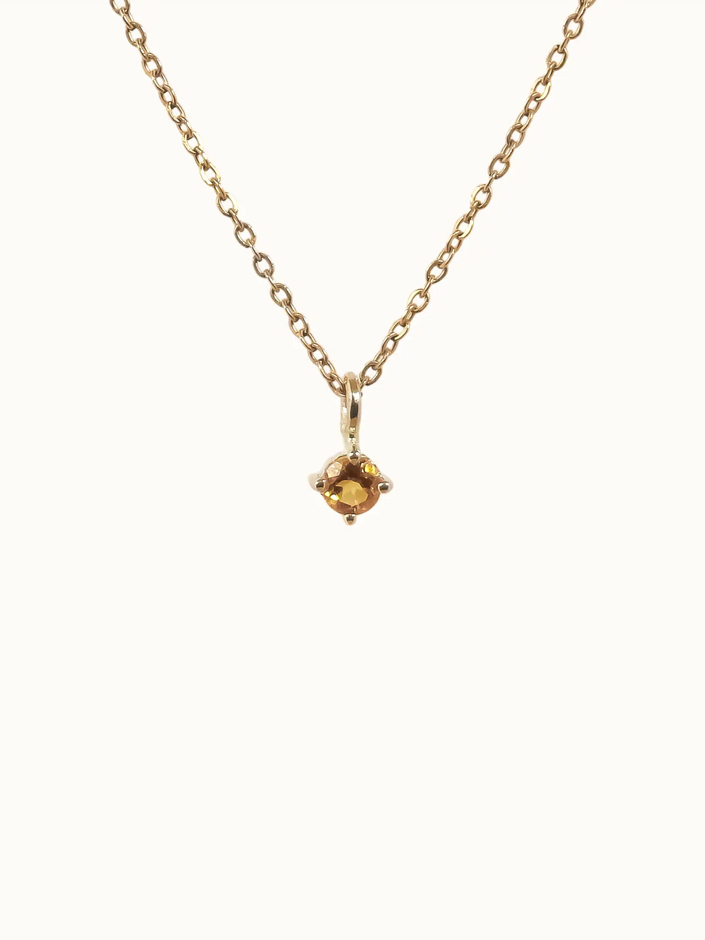 Gold necklace with a small yellow gemstone pendant on a white background