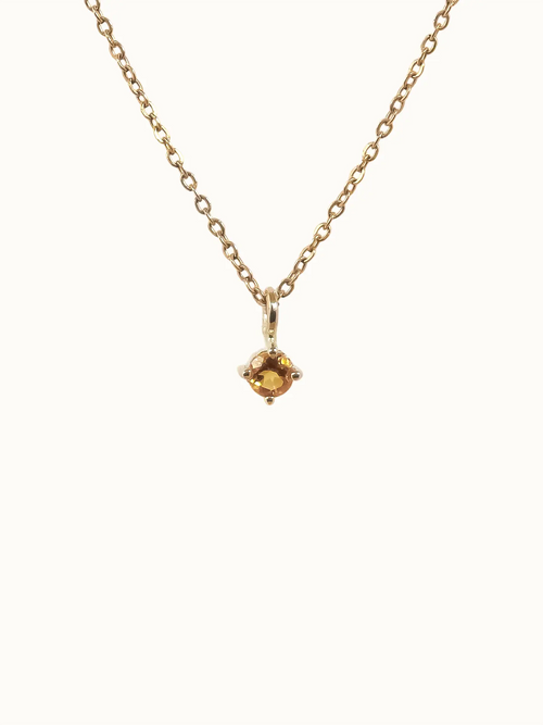 Gold necklace with a small yellow gemstone pendant on a white background