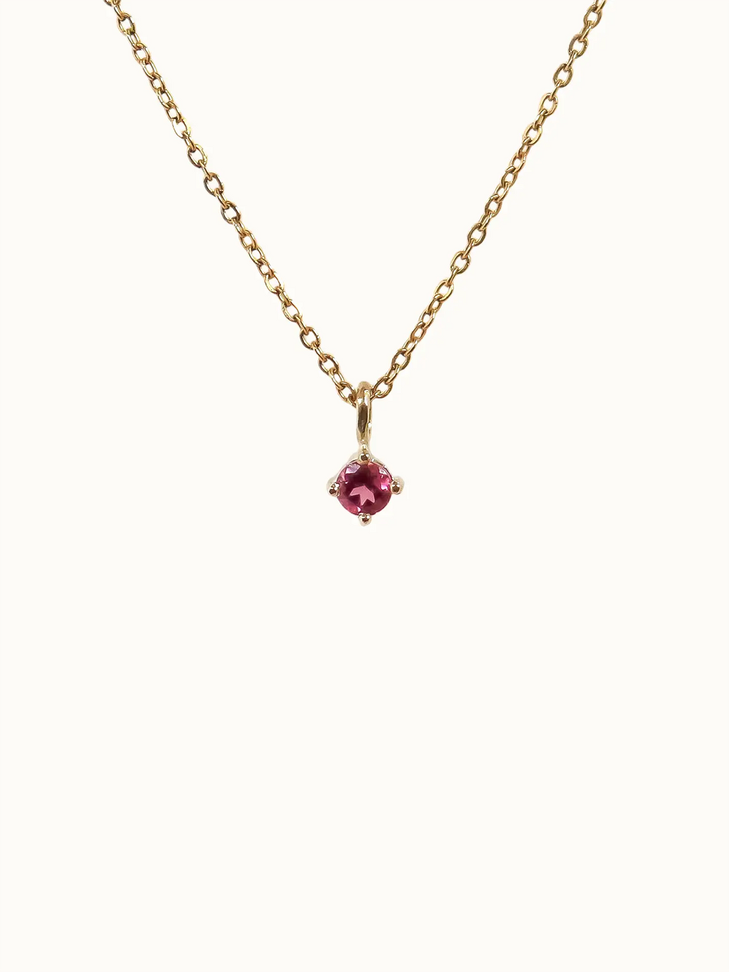 Gold necklace with a red gemstone pendant on a white background