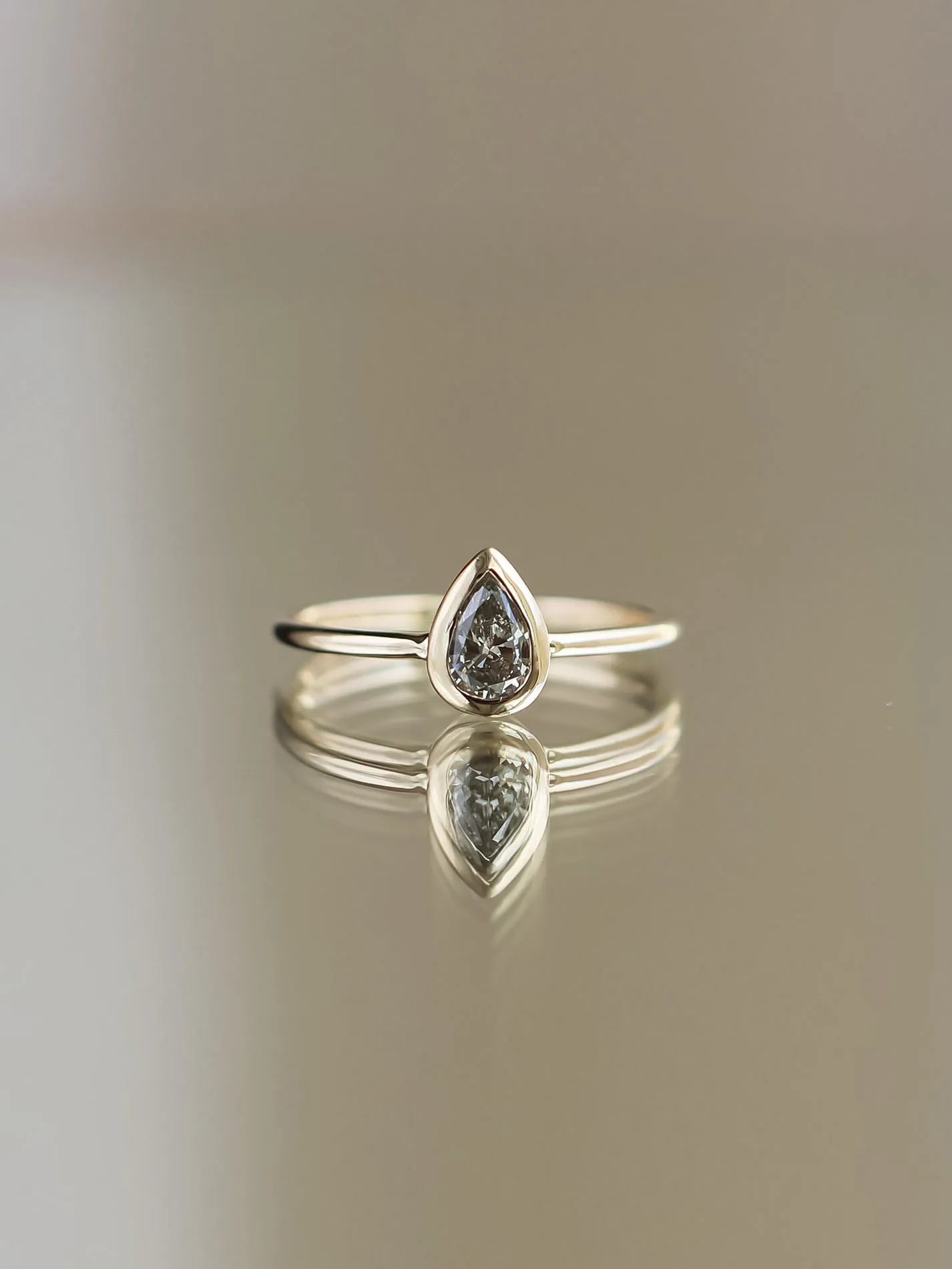 Silver ring with a teardrop-shaped diamond on a reflective surface.