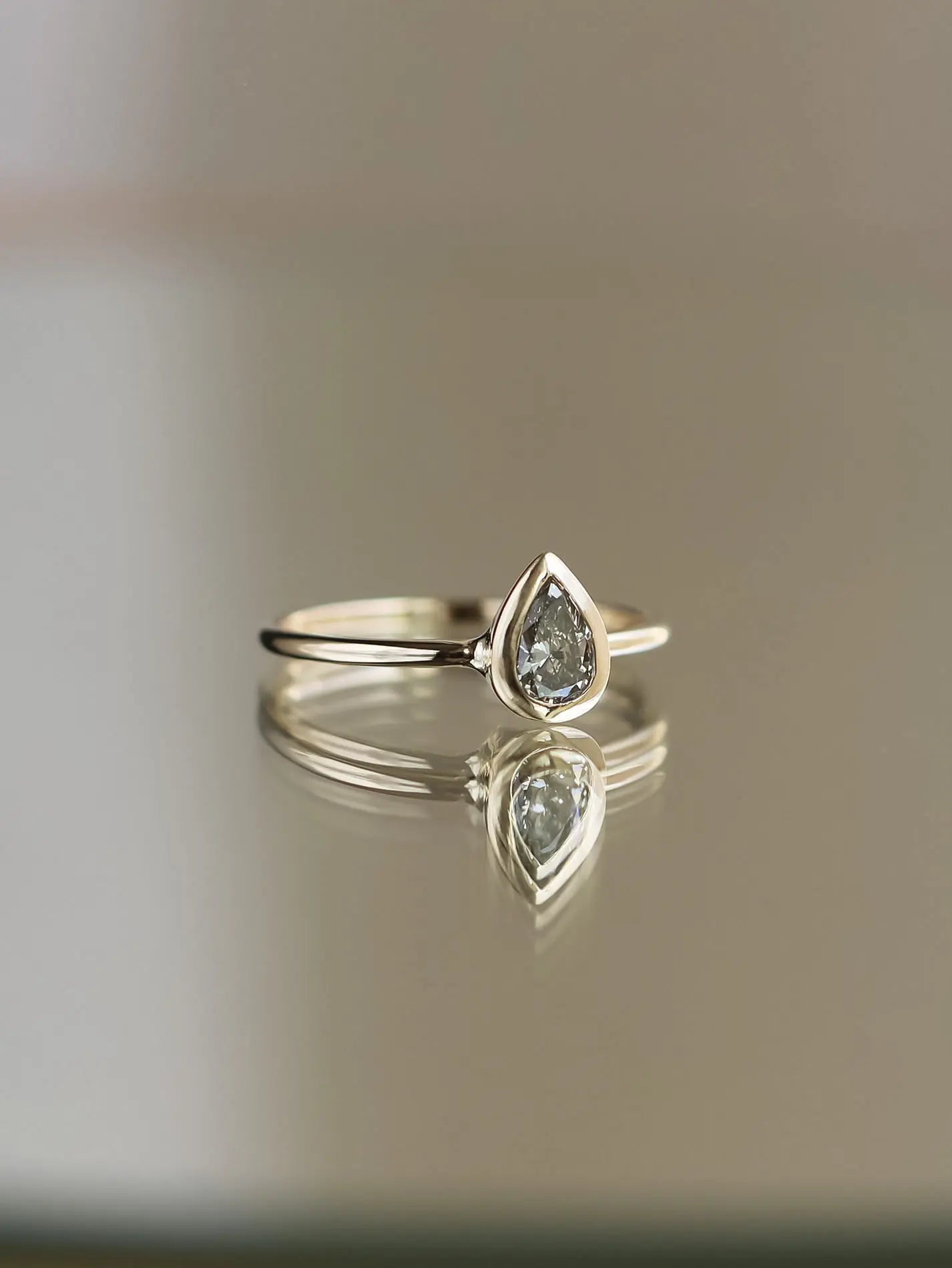 Teardrop-shaped diamond ring on a reflective surface with a neutral background