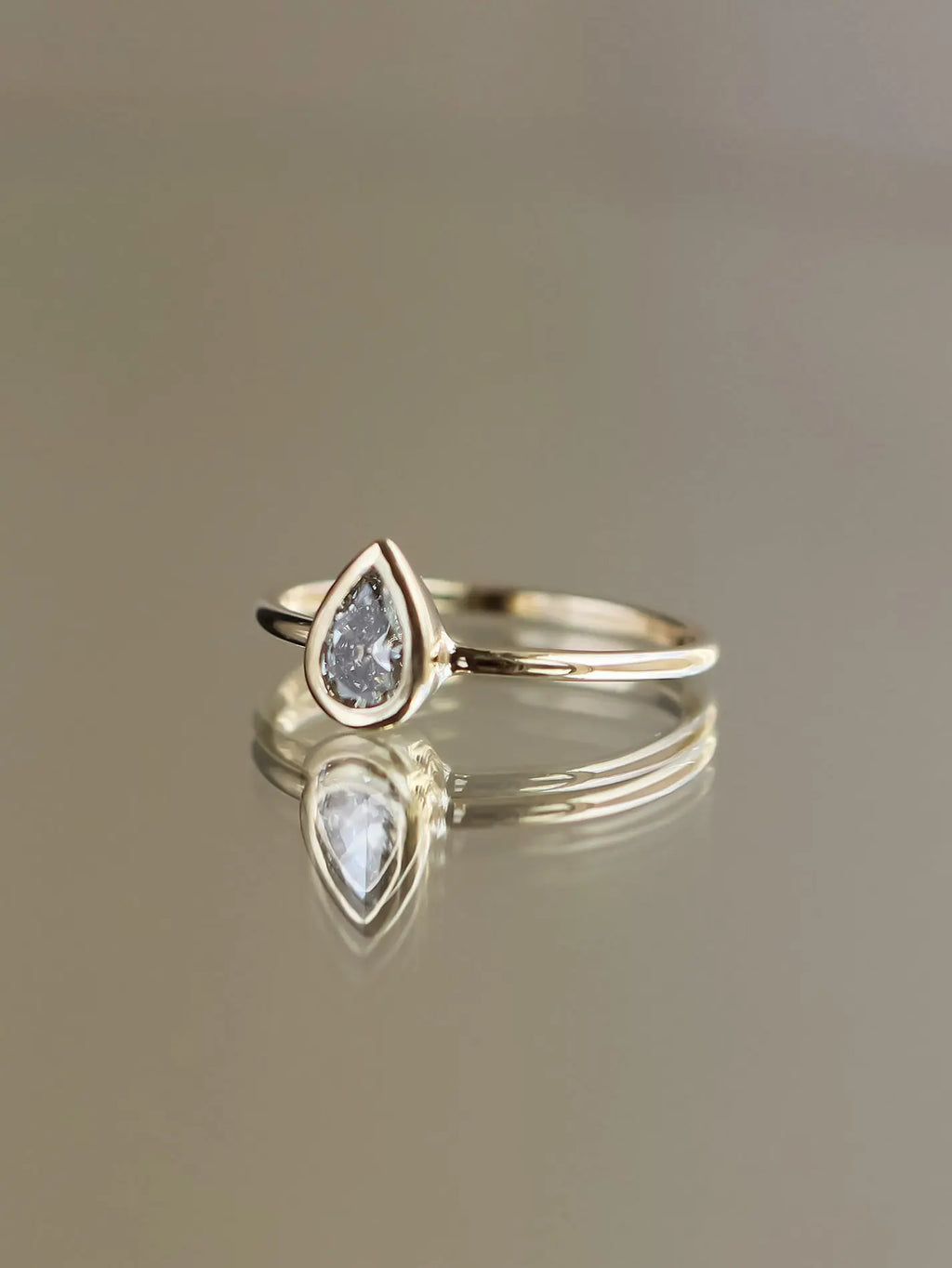 Gold ring with a teardrop-shaped gemstone on a reflective surface.
