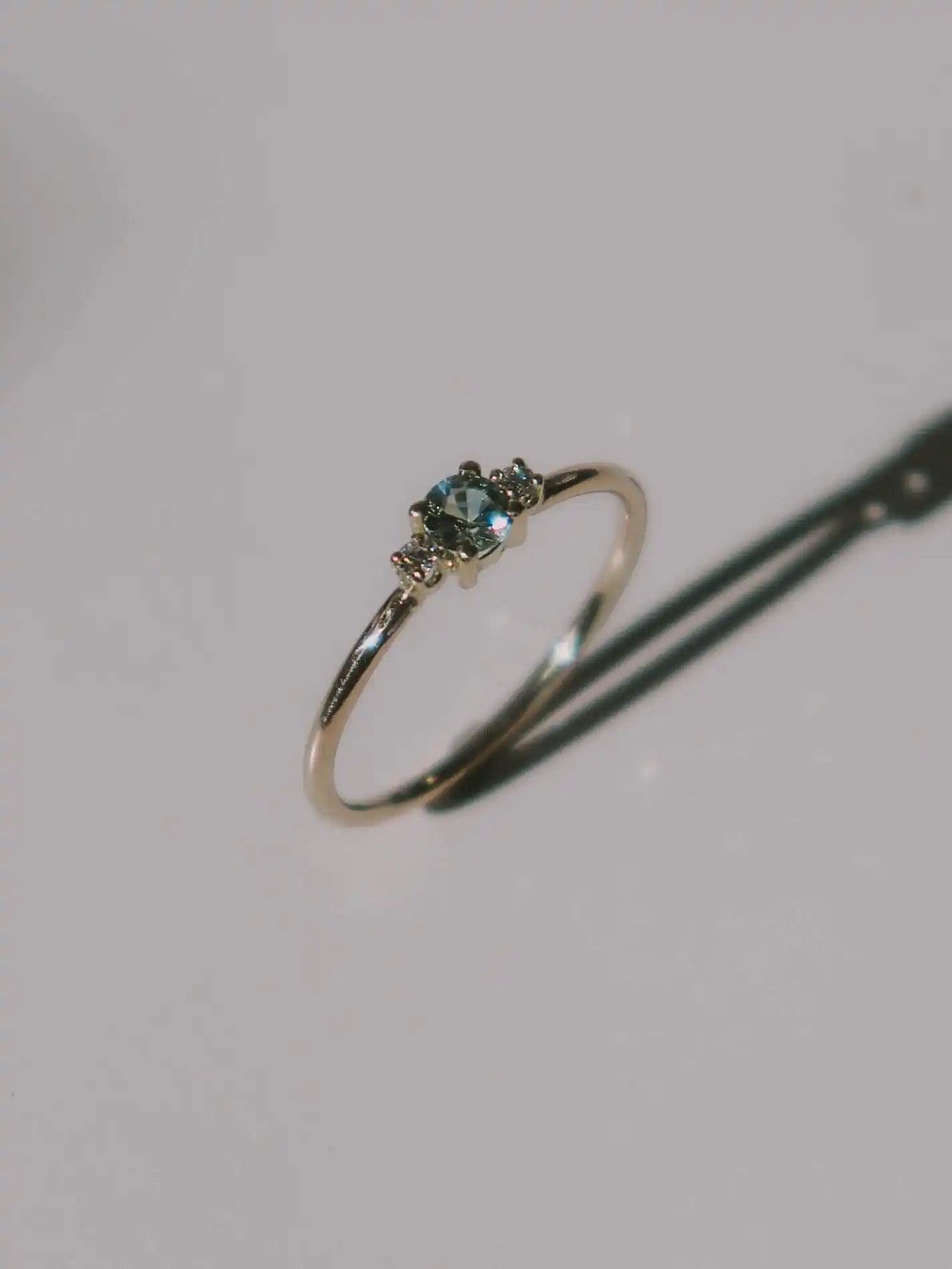 A classic teal blue green three-stone Sapphire ring with diamond accents.