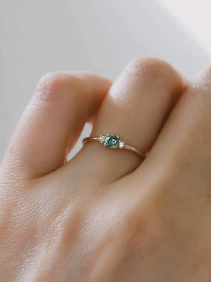 A classic teal blue green three-stone Sapphire ring with diamond accents.
