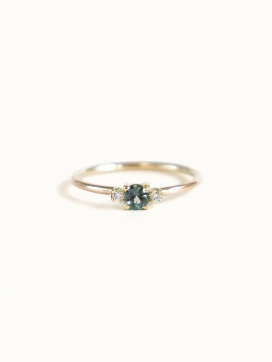 A classic teal blue green three-stone Sapphire ring with diamond accents.